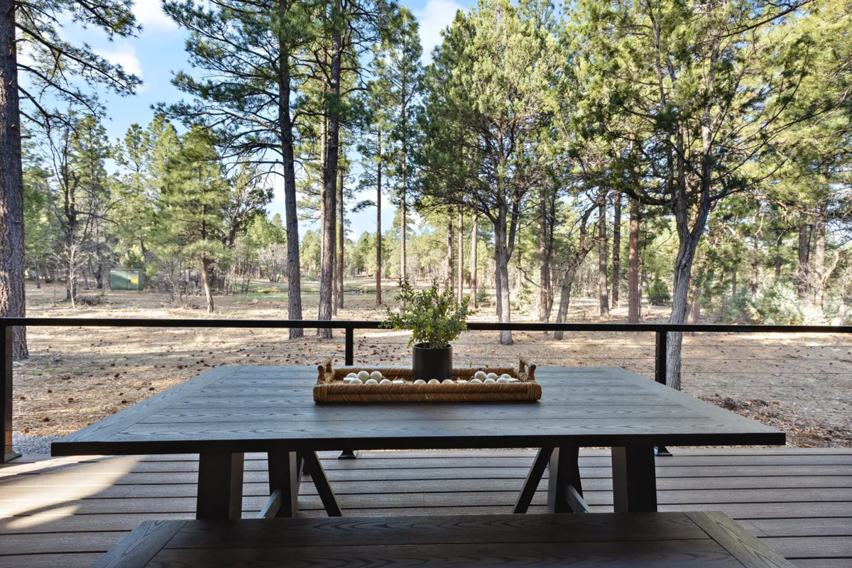 An outdoor dining table with a flower arrangement sits beneath the trees, offering a peaceful setting for lunches or outdoor meetings. The surrounding greenery and tranquil mood suggest opportunities to enjoy meals, listen to birdsong, or simply recharge between tasks.