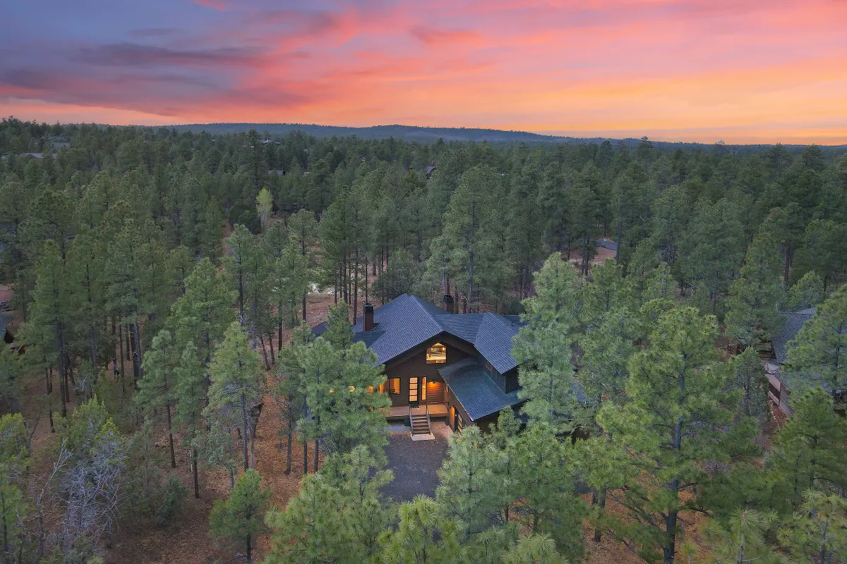 This image features the house nestled among tall trees during sunset, with a tranquil and inviting porch that overlooks the surrounding natural beauty. The peaceful setting highlights both the nearby forest and the promise of outdoor relaxation, perfectly capturing the atmosphere of a retreat connected with nature.