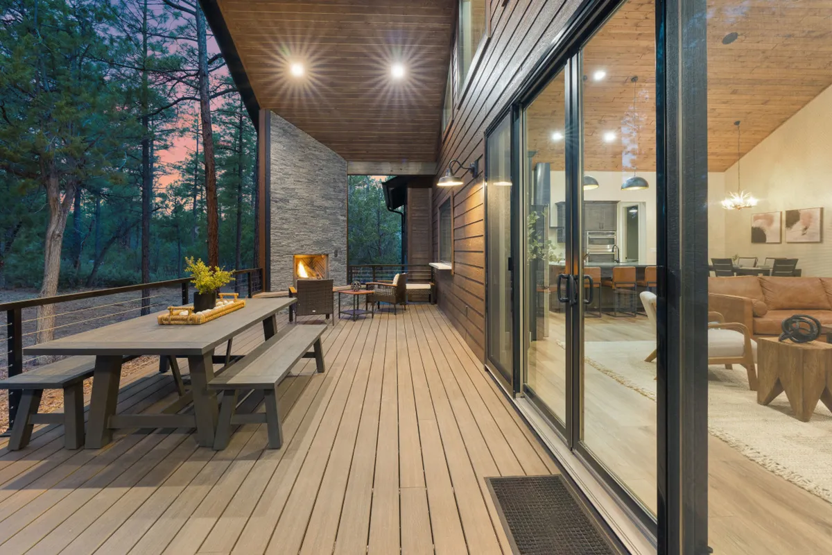 An inviting outdoor dining area features a table and chairs set on a patio, complemented by a cozy fireplace. The seating area is nestled among trees, creating a peaceful woodland vibe ideal for outdoor meals and gatherings.