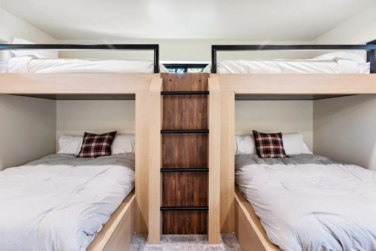 A playful bunk room featuring twin-over-full bunk beds with a sturdy ladder and plaid pillows. The space feels inviting and fun, designed for sleepovers, storytelling, and shared moments among children or friends.