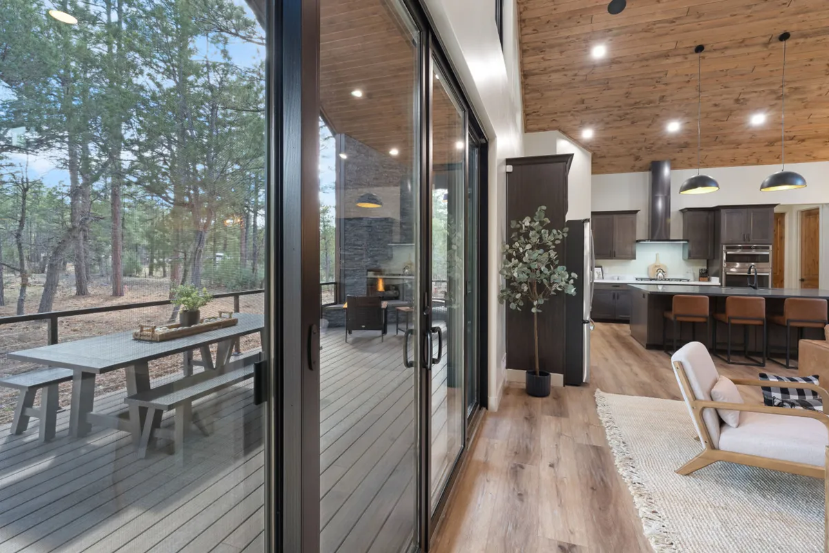 This photo presents a bright dining area set beside large glass doors, with a spacious table perfect for group meals. The adjacent kitchen island and sightline to the outdoors create a fluid transition from inside dining to nature, enhancing the inviting, communal atmosphere.