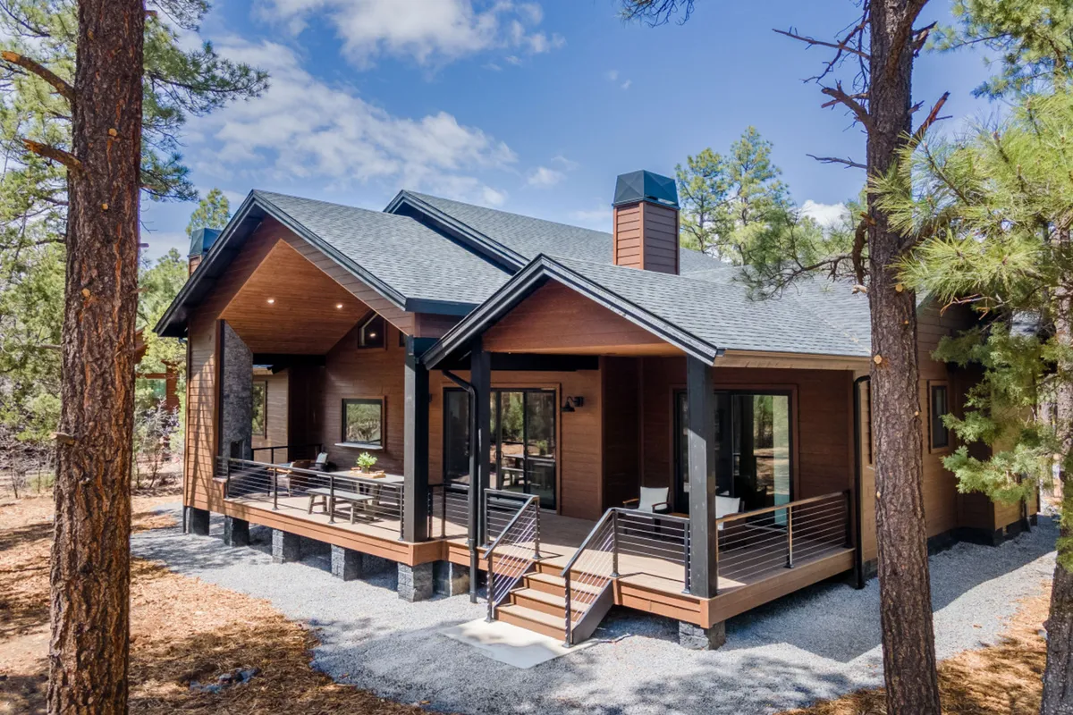 A modern cabin is highlighted amid tall pine trees, with a spacious porch extending into the forested landscape. The architecture blends seamlessly with nature, suggesting a calming and secluded environment that supports productivity and creativity.
