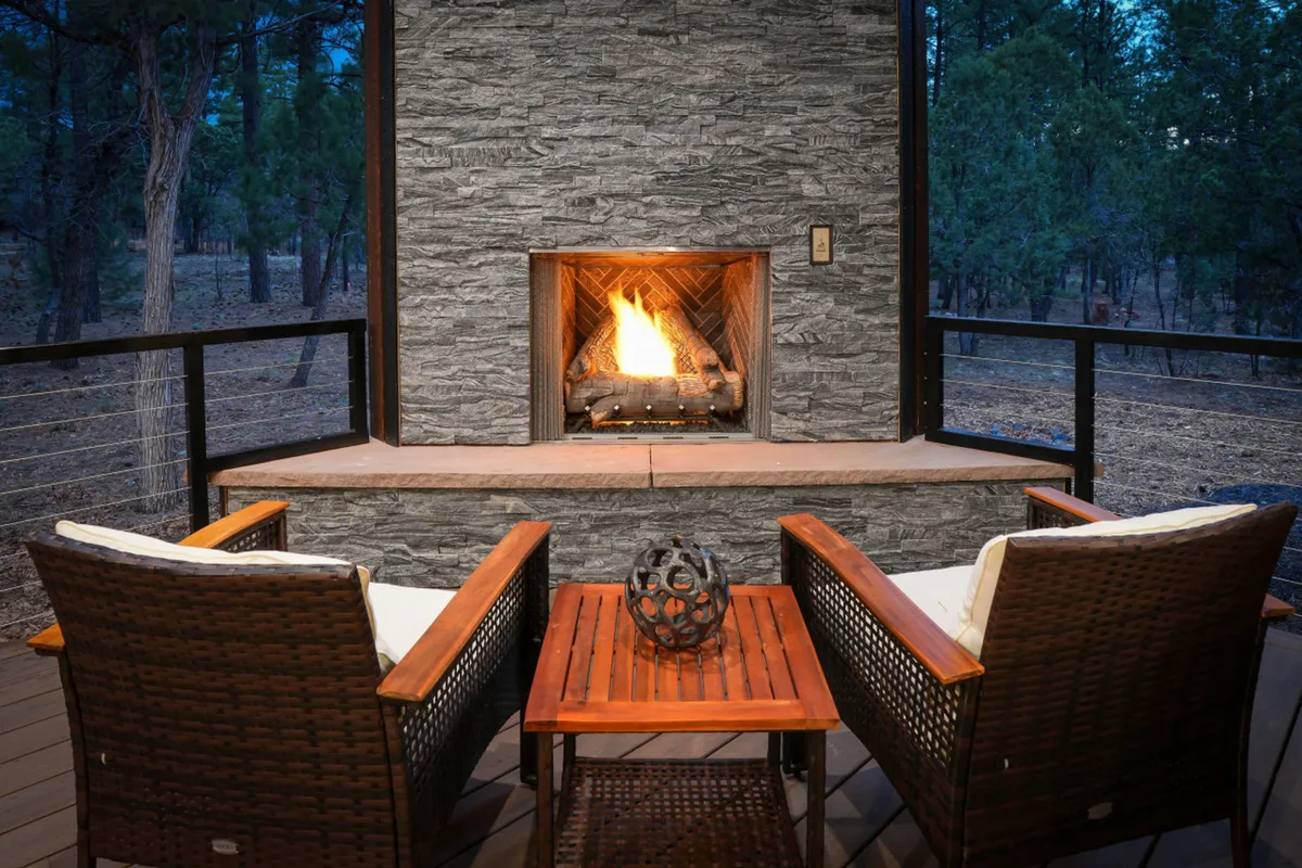 A cozy outdoor seating area centers around a decorative table and fireplace, surrounded by natural greenery. The ambiance is inviting, perfect for intimate evenings or simply unwinding after a day of adventure.