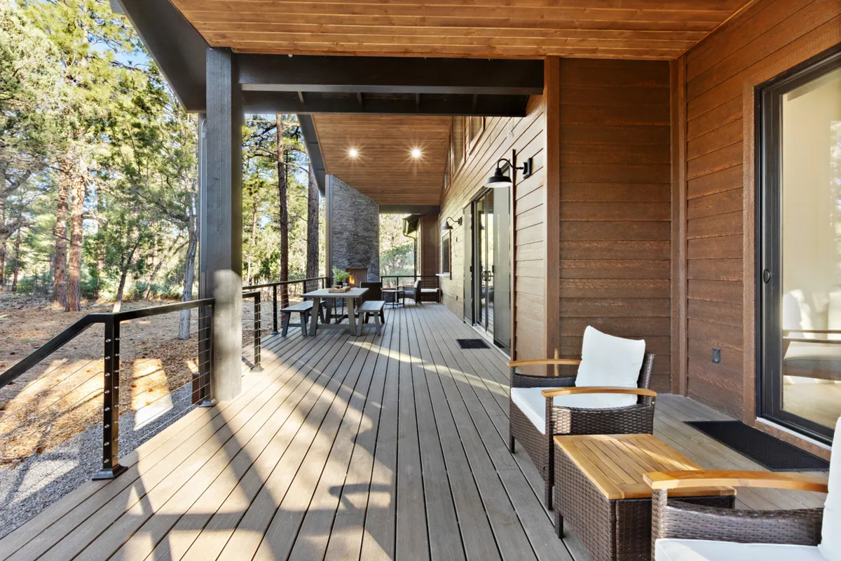 A wooden deck set with outdoor furniture and a dining table, bordered by a sturdy railing and immersed in the greenery of surrounding trees. The view extends into the quiet woods, creating an ideal spot for outdoor dining, wildlife observation, or simply soaking up the tranquil atmosphere.